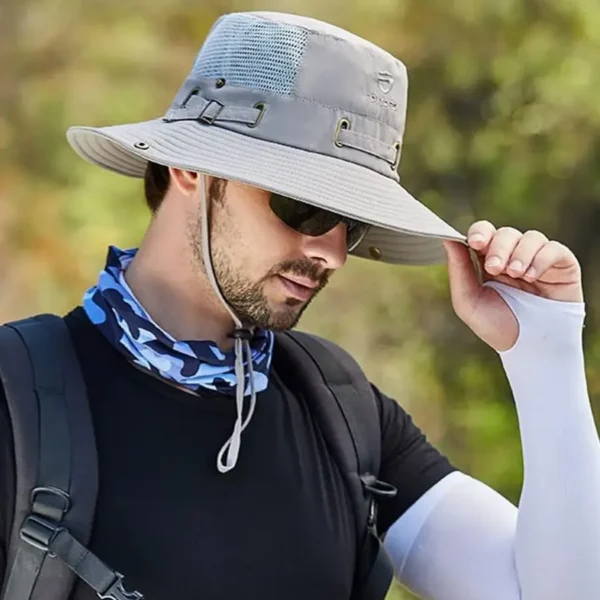 bob-avec-ficelle-pour-homme-gris Un homme de profil tient la visière de son bob chapeau dans un décor de nature flouté