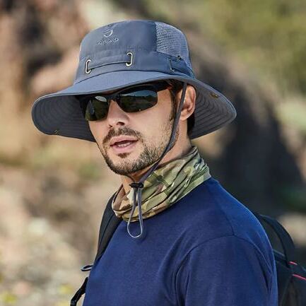 chapeau-soleil-pour-homme Un homme porte des lunettes de soleil et un bob chapeau dans un décor de nature flouté