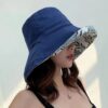 bob-chapeau-femme-bleu Une femme porte un bob chapeau élégant bleu marine sur un décor clair et lumineux