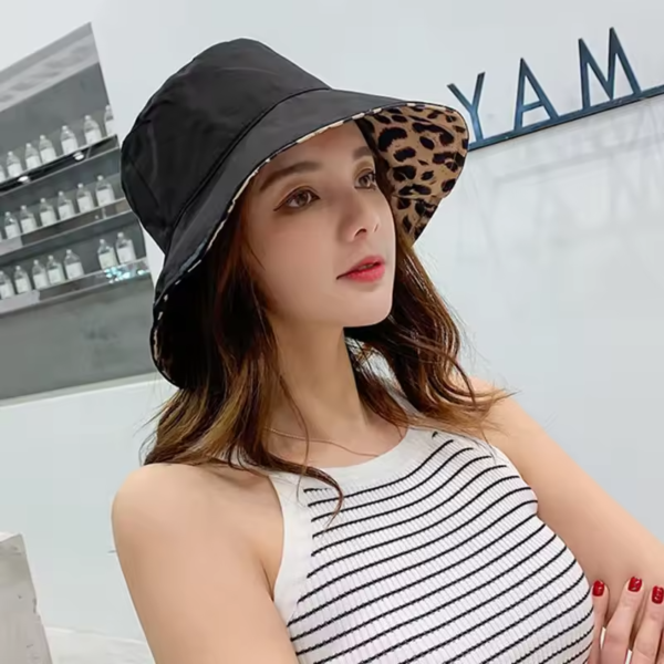 bob-reversible-femme Une femme porte un bob chapeau réversible noir avec une doublure style léopard sur un décor grisé