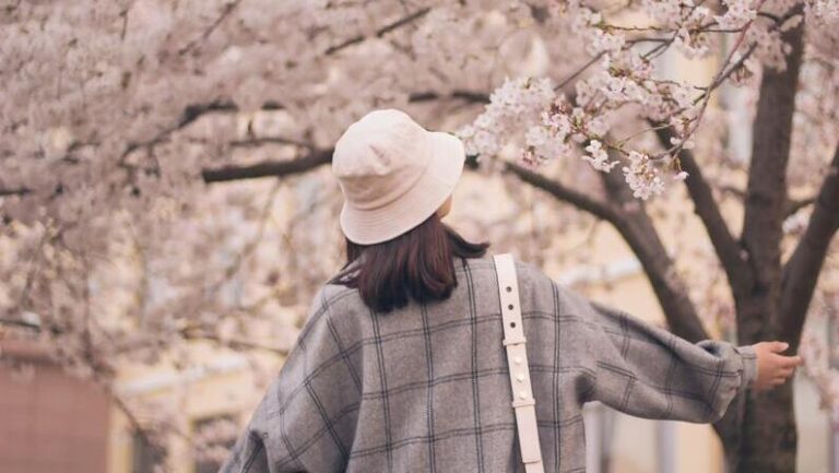 femme-qui-porte-un-bob-chapeau-flâne-au-milieu-des-arbres-en-fleur-au-printemps