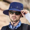 bob-peche-homme-femme Un modèle avec des lunettes noires de soleil porte un joli chapeau bob pêche couleur bleu marine sur la tête sur un décor de nature flouté