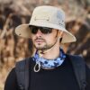 bob-pecheur-hommes-femmes Un pêcheur avec des lunettes noires de soleil porte un joli chapeau bob pêche beige sur la tête sur un décor de nature flouté