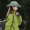 Une femme de profil porte un bob chapeau style cowboy vert avec ficelle sur un décor de nature