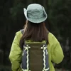 Une femme de dos porte un bob chapeau style cowboy vert avec ficelle sur un décor de nature