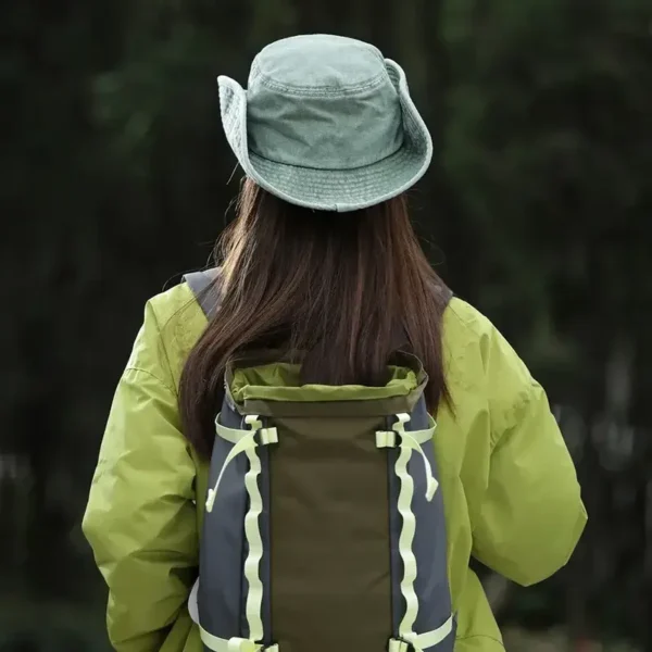 Une femme de dos porte un bob chapeau style cowboy vert avec ficelle sur un décor de nature