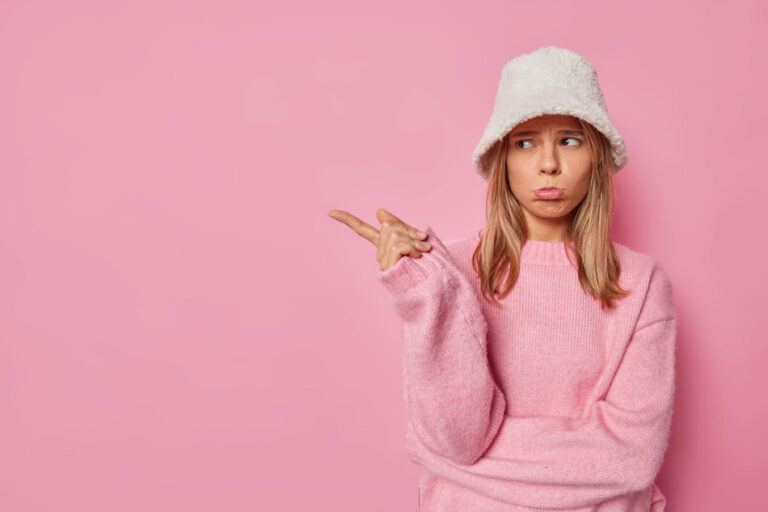 Fille porte un bob original sur la tête et a un visage qui fait une expression d'interrogation le fond est de couleur rose bonbon
