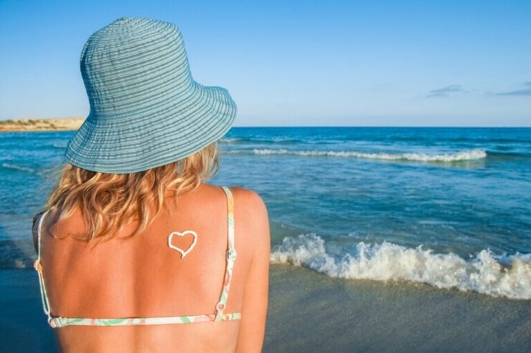 Femme de dos au bord de mer se protège les cheveux grâce à un bob chapeau bleu
