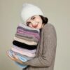 bonnet-epais-fourrure-femme Fille souriante porte un bonnet épais et doux pour l'hiver et porte aussi une pile d'autres bonnets de différentes couleurs pliés