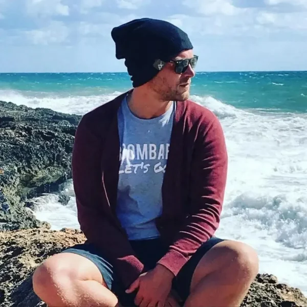 Un homme sur un décor de mer agité porte un bonnet et des lunettes