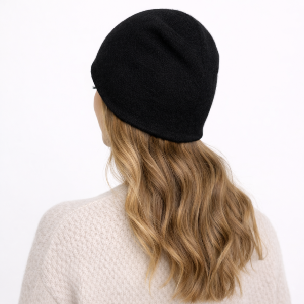 Une femme de dos porte un bonnet en cachemire noir sur un fond clair