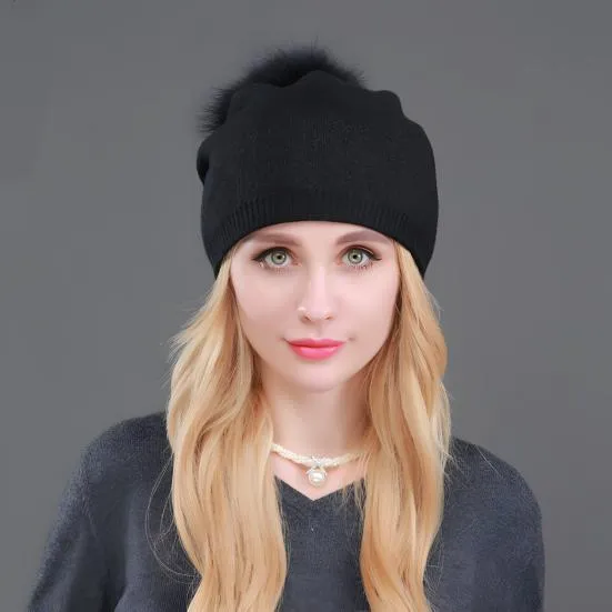 Un modèle féminin de face porte un bonnet à pompon noir sur un fond gris foncé