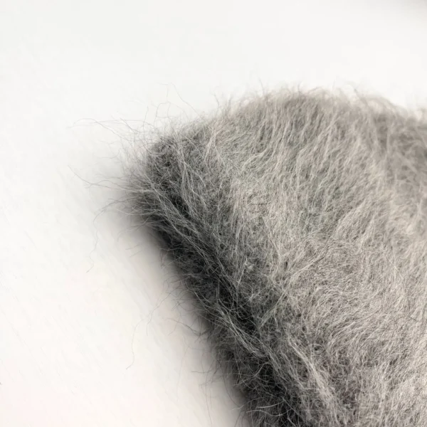 bonnet-gris-texture-duveteuse-grosse-maille Gros plan sur un bonnet en alpaga gris avec une texture duveteuse et poils longs, photographié sur fond blanc pour montrer la matière douce et chaude.
