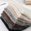 bonnet-laine-naturelle-empiles-couleurs-variees Pile de bonnets en alpaga pliés, montrant différentes teintes naturelles comme beige, gris, marron et noir, soulignant la douceur de la laine d’alpaga.