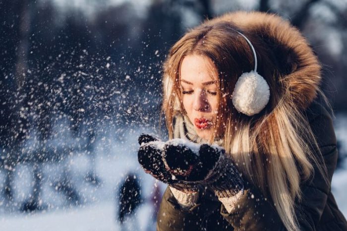 Jeune fille dans un paysage enneigé d'hiver porte un manteau en fourrure et des gants en laine et elle souffle dans de la neige